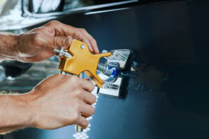 paintless dent repair tool. man fixing vehicle door with PDR technology
